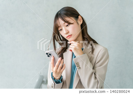 Depressed young Asian businesswoman in a suit holding a smartphone Depressed young Asian businesswoman in a suit holding a smartphone 140280024