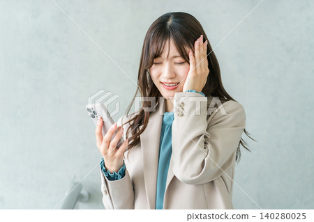 A young Asian businesswoman in a suit having trouble looking at her smartphone (failure, mistake, blunder, fraud) A young Asian businesswoman in a suit having trouble looking at her smartphone (failure, mistake, blunder, fraud) 140280025