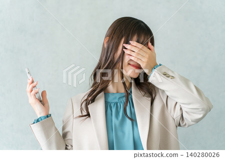 A young Asian businesswoman in a suit having trouble looking at her smartphone (failure, mistake, blunder, fraud) A young Asian businesswoman in a suit having trouble looking at her smartphone (failure, mistake, blunder, fraud) 140280026