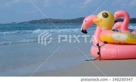 Large pink inflatable flamingo float standing on sandy beach with sea waves and tropical island landscape in background. Beach leisure concept Large pink inflatable flamingo float standing on sandy beach with sea waves and tropical island landscape in background. Beach leisure concept 140280347