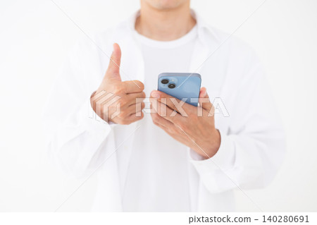 一位身穿白襯衫的中年男子在白色背景前豎起大拇指，同時舉起智慧型手機。 140280691