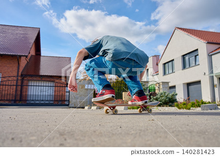 Teenager skateboarding on suburban street with houses in the background Teenager skateboarding on suburban street with houses in the background 140281423