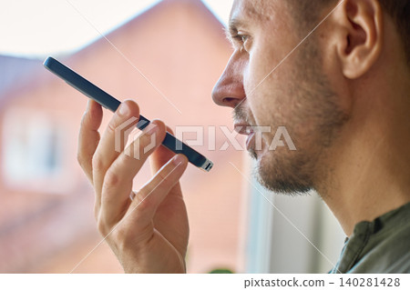 Closeup of man speaking into smartphone by window Closeup of man speaking into smartphone by window 140281428