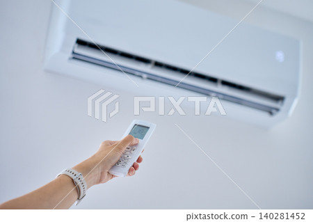 Person adjusting air conditioner with remote control Person adjusting air conditioner with remote control 140281452