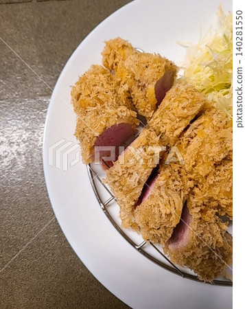 Crispy tonkatsu, a Japanese-style breaded and deep-fried pork cutlet, served with shredded cabbage and drizzled with savory sauce. A delightful balance of crunchy texture and juicy meat. 140281550