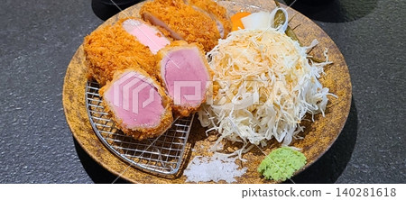 Crispy tonkatsu, a Japanese-style breaded and deep-fried pork cutlet, served with shredded cabbage and drizzled with savory sauce. A delightful balance of crunchy texture and juicy meat. 140281618