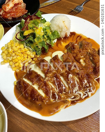 Crispy tonkatsu, a Japanese-style breaded and deep-fried pork cutlet, served with shredded cabbage and drizzled with savory sauce. A delightful balance of crunchy texture and juicy meat. 140281631