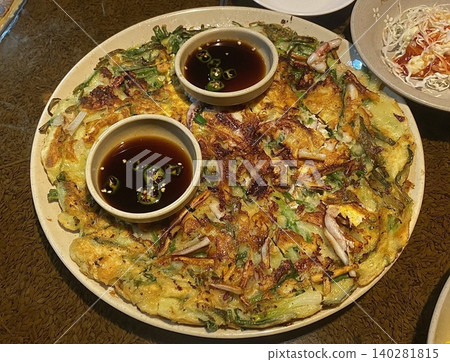 Pajeon is a savory Korean pancake made with green onions (pa) in a light batter, often mixed with seafood like squid or shrimp. Crispy on the outside and soft inside, it’s a flavorful side dish. 140281815
