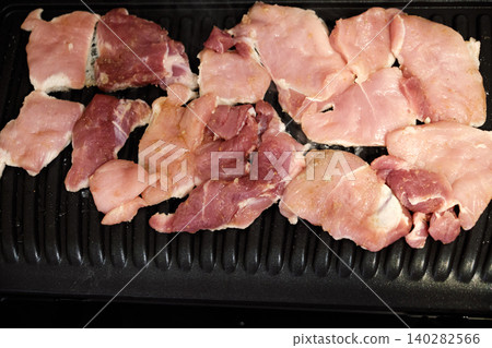 Raw pork slices on electric grill ribbed surface close up 140282566