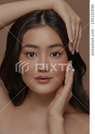 Beautiful portrait of an attractive japanese sensual young woman with a healthy clean skin and long brunette hair, touching her face standing isolated on a beige background Beautiful portrait of an attractive japanese sensual young woman with a healthy clean skin and long brunette hair, touching her face standing isolated on a beige background 140282696
