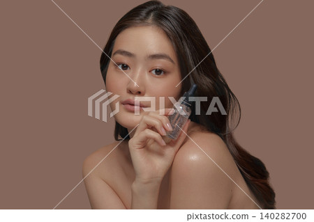 Charming asian ethnicity young model with a fresh smooth skin holding face moisturizer serum on a beige background Charming asian ethnicity young model with a fresh smooth skin holding face moisturizer serum on a beige background 140282700