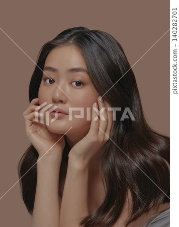 Beautiful portrait of an attractive japanese sensual young woman with a healthy clean skin and long brunette hair, touching her face standing isolated on a beige background Beautiful portrait of an attractive japanese sensual young woman with a healthy clean skin and long brunette hair, touching her face standing isolated on a beige background 140282701