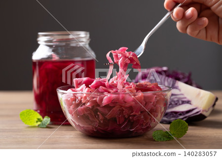 Hand holding fork and eating red cabbage sauerkraut in a glass bowl Hand holding fork and eating red cabbage sauerkraut in a glass bowl 140283057