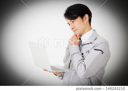 一位身穿灰色工作服的中年商人,在白色背景前,正看著他的筆記型電腦,若有所思。 一位身穿灰色工作服的中年商人,在白色背景前,正看著他的筆記型電腦,若有所思。 140283210