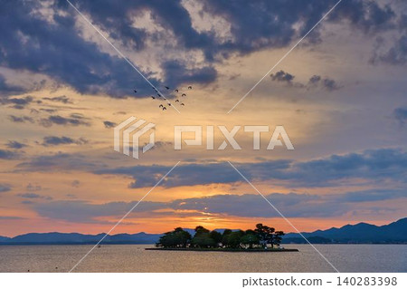 A view to the northwest from the shores of Lake Shinji in Sodeshi-cho, Matsue City, Shimane Prefecture, famous for its sunsets (including Yomegashima Island, a heron in flight, and the mountains of the Shimane Peninsula). A view to the northwest from the shores of Lake Shinji in Sodeshi-cho, Matsue City, Shimane Prefecture, famous for its sunsets (including Yomegashima Island, a heron in flight, and the mountains of the Shimane Peninsula). 140283398