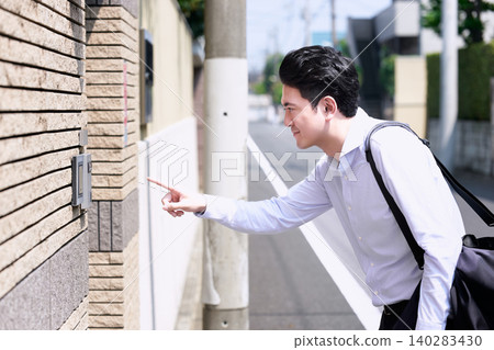 A Japanese man in his 30s, working in sales, presses the intercom button of a house in a residential area. A Japanese man in his 30s, working in sales, presses the intercom button of a house in a residential area. 140283430