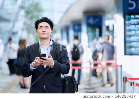 A Japanese man in his 30s, a company employee, was at the bus terminal with his smartphone, checking bus schedules. 140283437