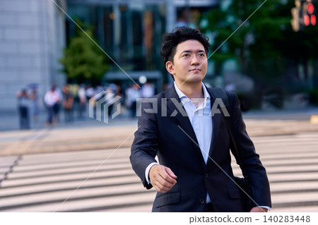 一位三十多歲的日本商人,在晚間尖峰時段走過辦公區十字路口的行人穿越道。 一位三十多歲的日本商人,在晚間尖峰時段走過辦公區十字路口的行人穿越道。 140283448