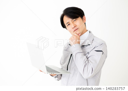 一位身穿灰色工作服的中年商人,在白色背景前,正看著他的筆記型電腦,若有所思。 一位身穿灰色工作服的中年商人,在白色背景前,正看著他的筆記型電腦,若有所思。 140283757
