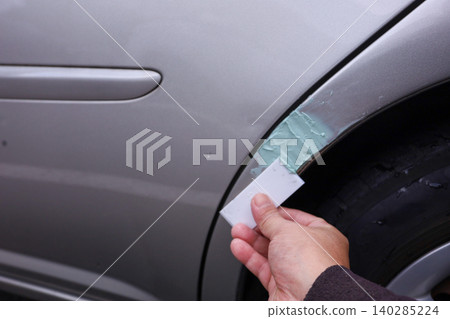 用膩子修補汽車擋泥板上的刮痕。 140285224
