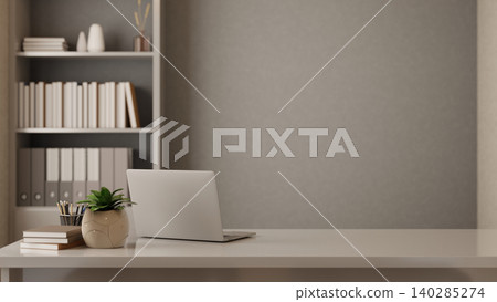 Laptop with book and pencil beside potted plant on white table in front of shelf in grey wall office Laptop with book and pencil beside potted plant on white table in front of shelf in grey wall office 140285274