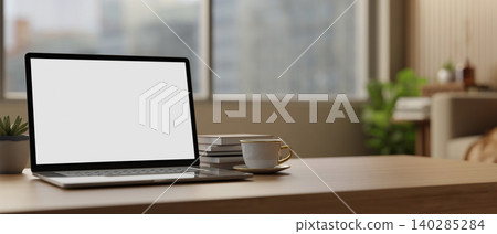 White screen laptop with books and coffee cup on wooden table across glass window in the living room White screen laptop with books and coffee cup on wooden table across glass window in the living room 140285284