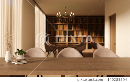Wooden table with books and potted plant and chairs across bookshelf with chandelier in the library. 140285294