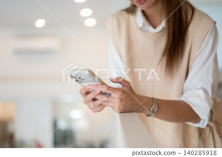 Close up of a woman looking at phone holding with both hands standing in cafe or living room at home Close up of a woman looking at phone holding with both hands standing in cafe or living room at home 140285918