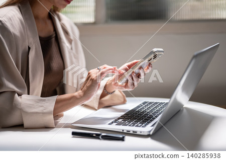 Close up of woman's hands holding and touching on phone over laptop beside pen while sitting in cafe Close up of woman's hands holding and touching on phone over laptop beside pen while sitting in cafe 140285938
