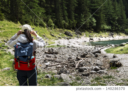 Traveler with backpack looking at mountain lake in the Austrian Alps, highlighting exploring remote mountain landscapes Traveler with backpack looking at mountain lake in the Austrian Alps, highlighting exploring remote mountain landscapes 140286370