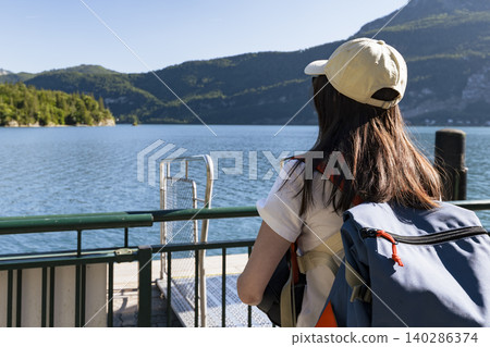 Young woman looking at the lake and mountains from a pier at Wolfgangsee in the Austrian Alps, expressing a connection with nature 140286374