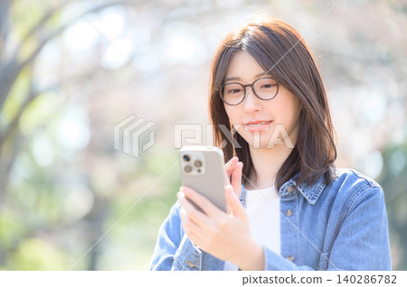 Japanese woman using her smartphone in a park Japanese woman using her smartphone in a park 140286782
