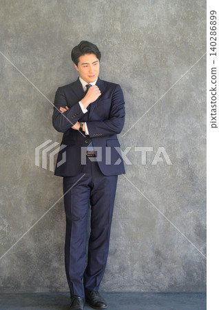 一位身穿西裝的日本男子雙手交叉,背景為灰色。 一位身穿西裝的日本男子雙手交叉,背景為灰色。 140286899