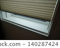 A beige pleated screen (honeycomb shade) installed on a small window. 140287424