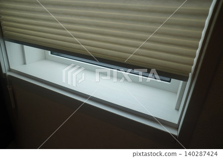 A beige pleated screen (honeycomb shade) installed on a small window. 140287424