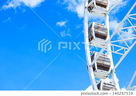 high cabin frame work large Ferris wheel structure amusement carousel set against a clear blue sky with scattered white clouds high cabin frame work large Ferris wheel structure amusement carousel set against a clear blue sky with scattered white clouds 140287519