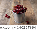 Juicy ripe fresh cherries with water drops in a miniature bucket on a wooden background. Seasonal fruits, harvest, in rustic style. Selective focus, close-up. 140287894