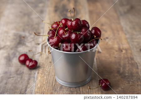 Juicy ripe fresh cherries with water drops in a miniature bucket on a wooden background. Seasonal fruits, harvest, in rustic style. Selective focus, close-up. Juicy ripe fresh cherries with water drops in a miniature bucket on a wooden background. Seasonal fruits, harvest, in rustic style. Selective focus, close-up. 140287894