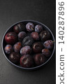 Juicy ripe fresh plum with water drops in gray plate on black background. Seasonal fruits. Selective focus, close-up. 140287896