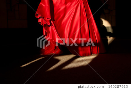 Cropped shot of a woman in a vibrant red silk dress moving in the dark. Elegant female legs or gown hem catching dramatic low key sunlight with long geometric shadows on the floor Cropped shot of a woman in a vibrant red silk dress moving in the dark. Elegant female legs or gown hem catching dramatic low key sunlight with long geometric shadows on the floor 140287913