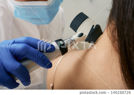 Mole dermatoscopy. Doctor examines the patient's mole with a dermatoscope for prevention of melanoma, close-up. 140288726