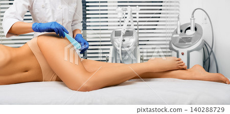 Legs hair laser removal. Beautician applies a special gel to legs before a laser hair removal procedure 140288729