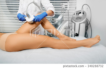 Woman's body slimming ultrasonic cavitation using ultrasound cavitation machine with a cosmetologist. Anti-cellulite therapy for female leg Woman's body slimming ultrasonic cavitation using ultrasound cavitation machine with a cosmetologist. Anti-cellulite therapy for female leg 140288732