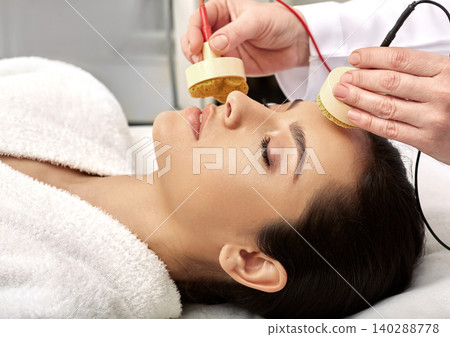 Facial microcurrent therapy. Microcurrent procedure for a female face at a beauty clinic, close-up Facial microcurrent therapy. Microcurrent procedure for a female face at a beauty clinic, close-up 140288778