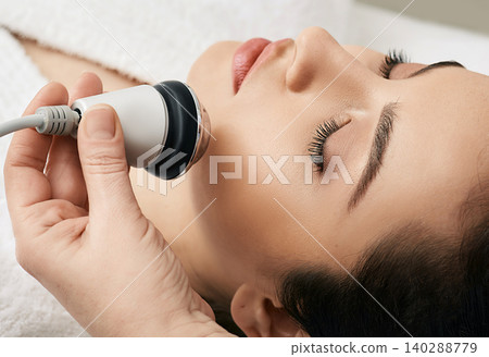 Brunette woman receiving radiofrequency lifting procedure for her face skin rejuvenation at aesthetic cosmetology clinic Brunette woman receiving radiofrequency lifting procedure for her face skin rejuvenation at aesthetic cosmetology clinic 140288779