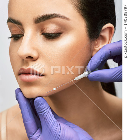 Mesothreads facial. Face contour lifting procedure, a needle with mesothreads near a female face, close-up Mesothreads facial. Face contour lifting procedure, a needle with mesothreads near a female face, close-up 140288797