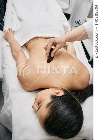 Gouache massage. Doctor doing a physical effect on woman's body using a gouache scraper for increased blood and lymph flow 140288804