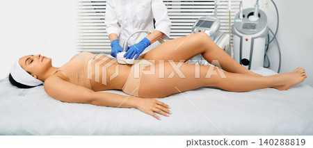 Beautiful woman having cavitation, procedure removing cellulite on her belly at beauty clinic Beautiful woman having cavitation, procedure removing cellulite on her belly at beauty clinic 140288819