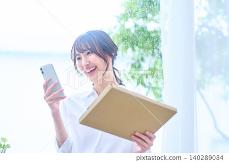 窗邊的一位女士收到了包裹,用智慧型手機查看後露出了笑容。 窗邊的一位女士收到了包裹,用智慧型手機查看後露出了笑容。 140289084