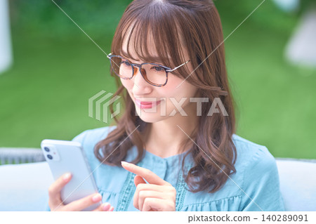 一名戴眼鏡的女子在戶外一邊指著一邊操作她的智慧型手機。 140289091